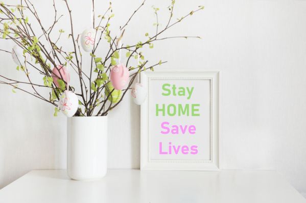 Easter concept 2020. Vase with birch tree branches with Easter eggs and frame with slogan - Stay at Home, Save Lives.